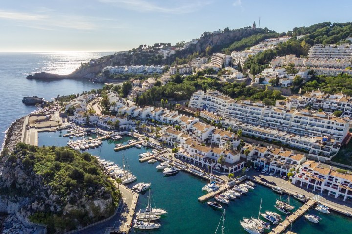 Aerial view of a coastal town with a marina and white buildings on a hillside.