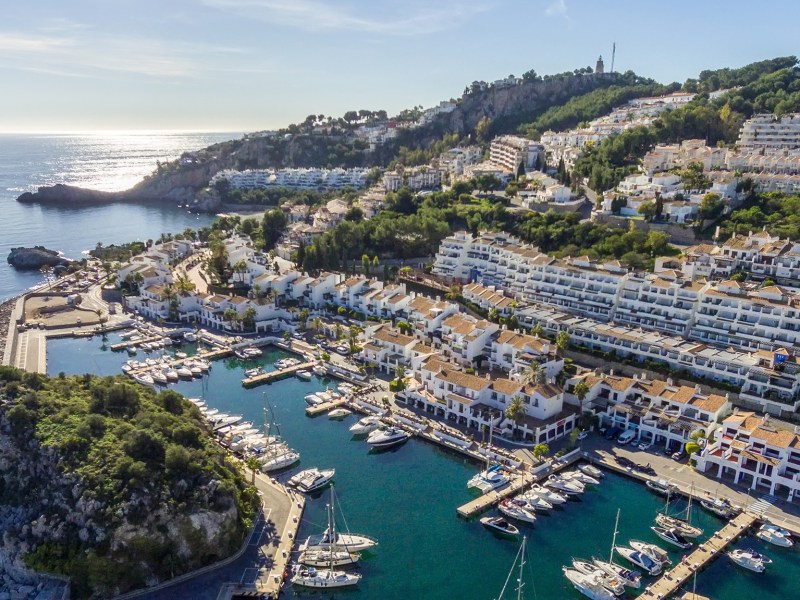 Aerial view of a coastal town with a marina and white buildings on a hillside.