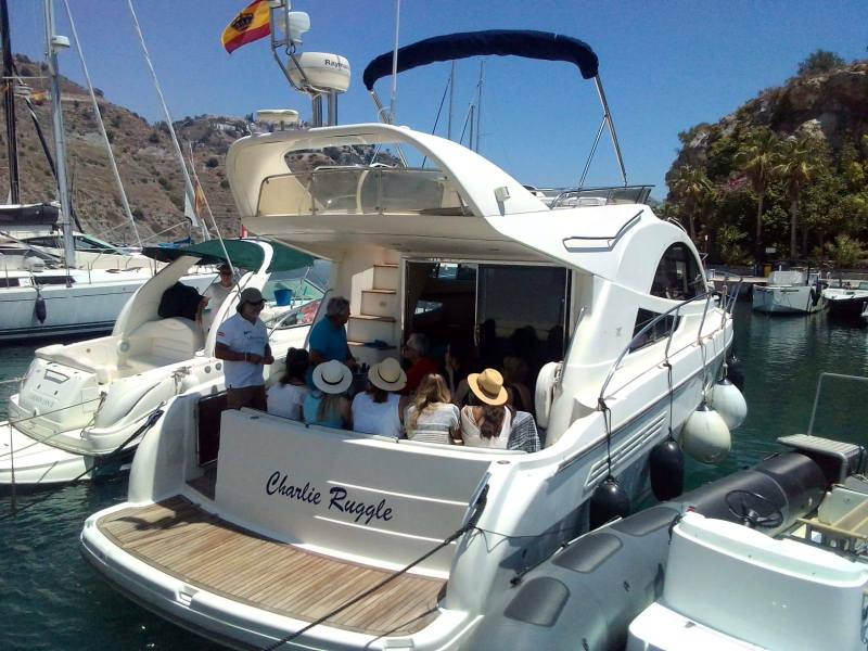 People sitting on a yacht in a marina with a Spanish flag.
