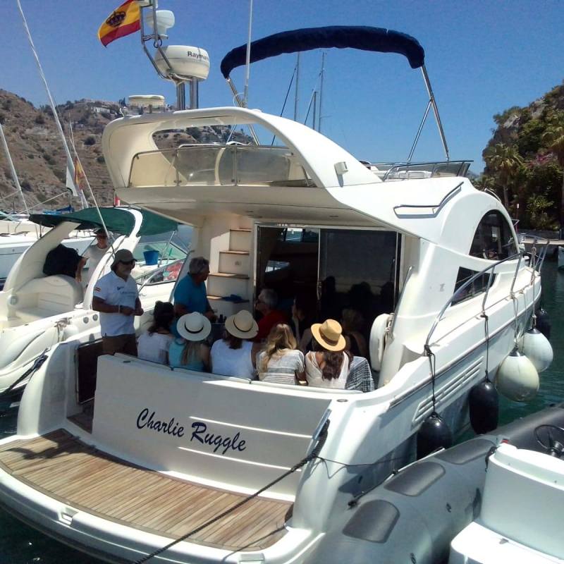 People sitting on a yacht in a marina with a Spanish flag.