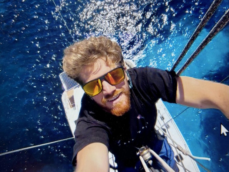Person in sunglasses taking a selfie on a boat mast, with blue ocean in the background.