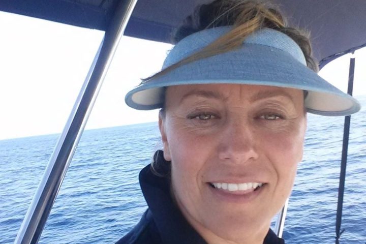 Woman in blue visor smiling on a boat with ocean in the background.