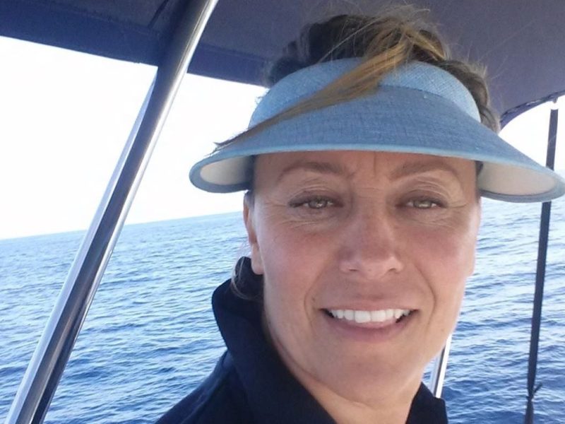 Woman in blue visor smiling on a boat with ocean in the background.