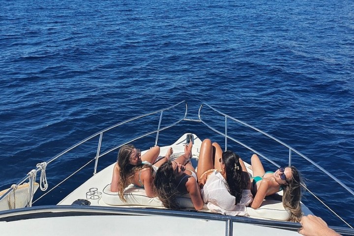 People sunbathing on the bow of a boat, surrounded by blue ocean.