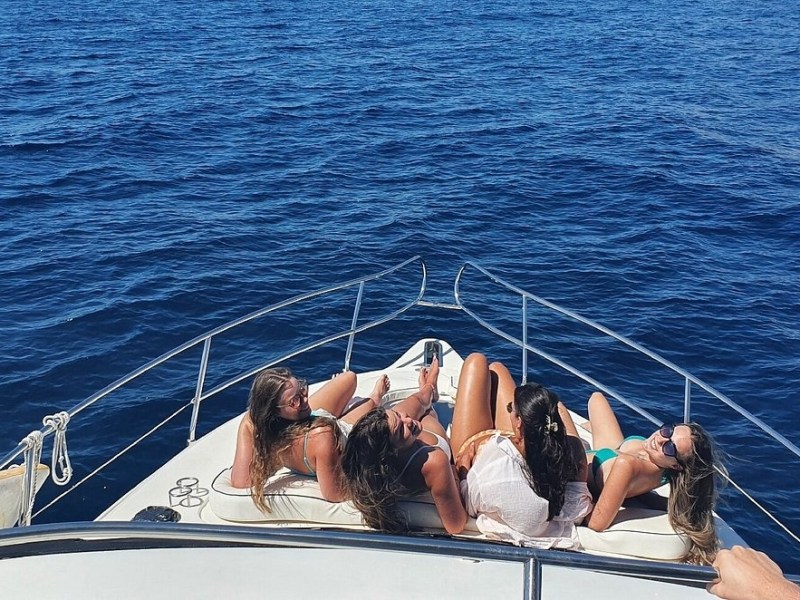 People sunbathing on the bow of a boat, surrounded by blue ocean.