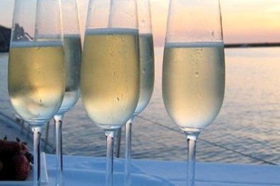Five champagne glasses on a table by a lake at sunset.