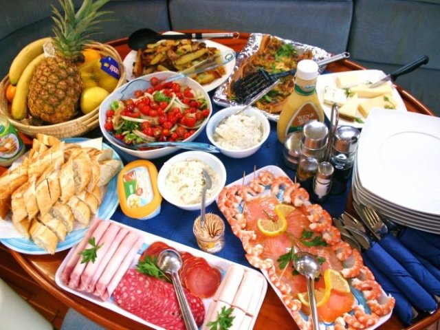 Assorted buffet with fruits, salads, breads, cold cuts, cheese, and condiments on a wooden table.