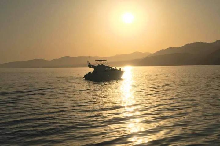 Boat on calm water at sunset with mountains in the background.