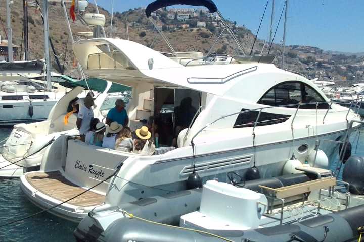 Group of people on a docked white yacht with hills and houses in the background.