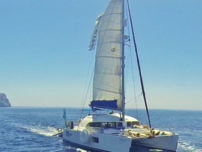 Sailboat with a large sail on the ocean under clear skies.