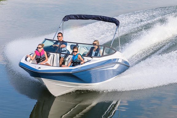 Family of four speeding on a blue and white boat, creating waves on a calm lake.