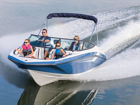 Family of four speeding on a blue and white boat, creating waves on a calm lake.
