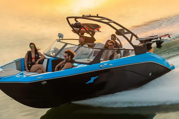 Five people on a blue speedboat cruising on water during sunset.