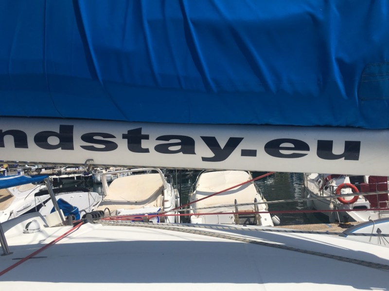 Blue boat sail with visible text 'ndstay.eu' above docked boats.