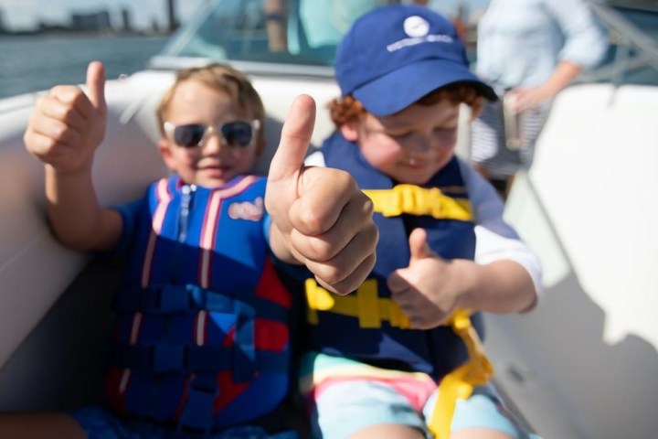 Two children in life jackets giving thumbs up on a boat.