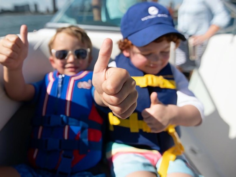 Two children in life jackets giving thumbs up on a boat.