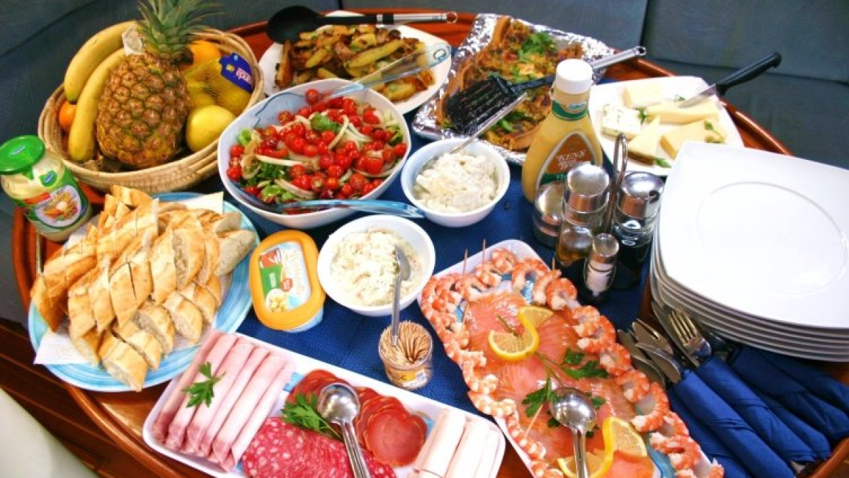 A table with assorted dishes, fruits, salads, bread, meats, and cheese on a blue tablecloth.