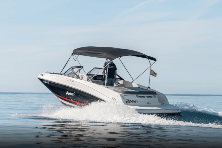 Motorboat with canopy speeding on calm water under clear sky.