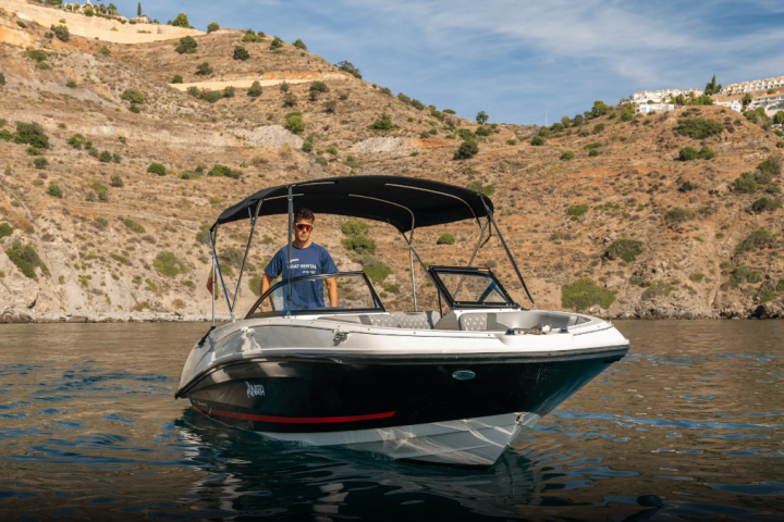 Person on a small motorboat in a calm lake with rocky hills in the background.