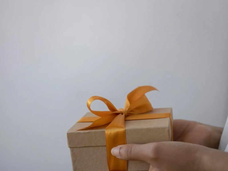 Hands holding a small gift box with an orange ribbon.