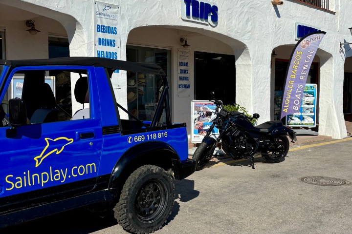 Blue jeep and black motorcycle parked outside a trips and boat rental shop.
