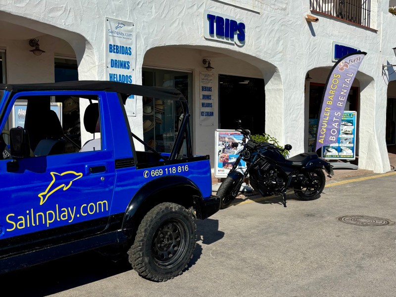 Blue jeep and black motorcycle parked outside a trips and boat rental shop.