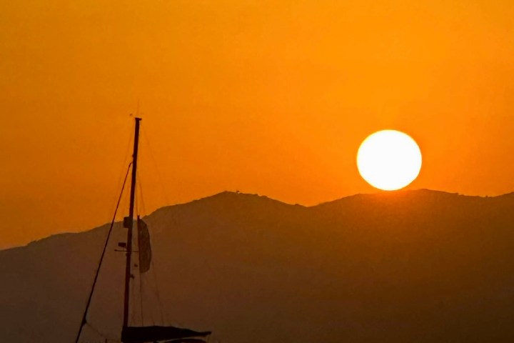 Silhouette of a boat on the water with a sunset behind mountains.