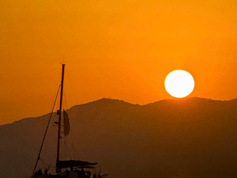 Silhouette of a boat on the water with a sunset behind mountains.