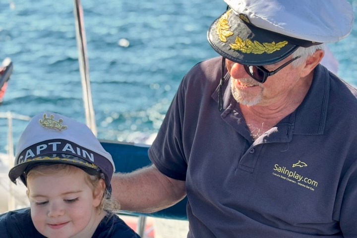 Child and elderly man wearing sailor hats on a boat with ocean in background.