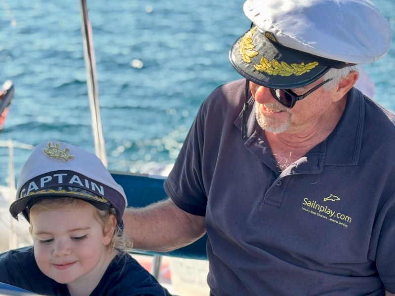 Child and elderly man wearing sailor hats on a boat with ocean in background.
