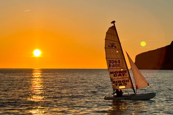 Sailboat on the water at sunset with golden sky and sun reflection.
