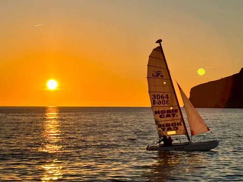 Sailboat on the water at sunset with golden sky and sun reflection.