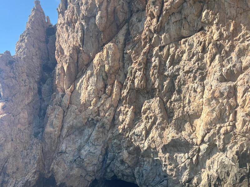 Kayaker near a large rocky cliff with a cave opening above blue water.