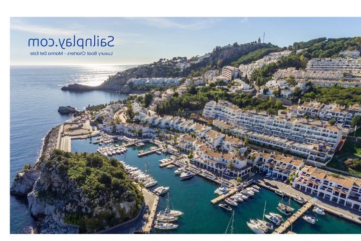 Aerial view of a coastal town with marina and hillside buildings near the sea.