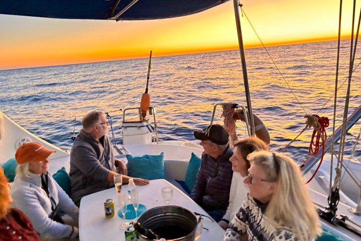 Group of people on a boat at sunset, sitting around a table with drinks.