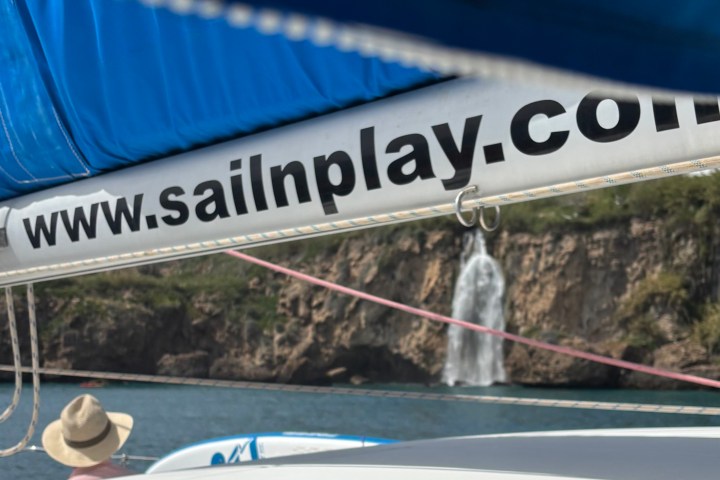 Sail with URL on boom above a waterfall and person wearing a hat.