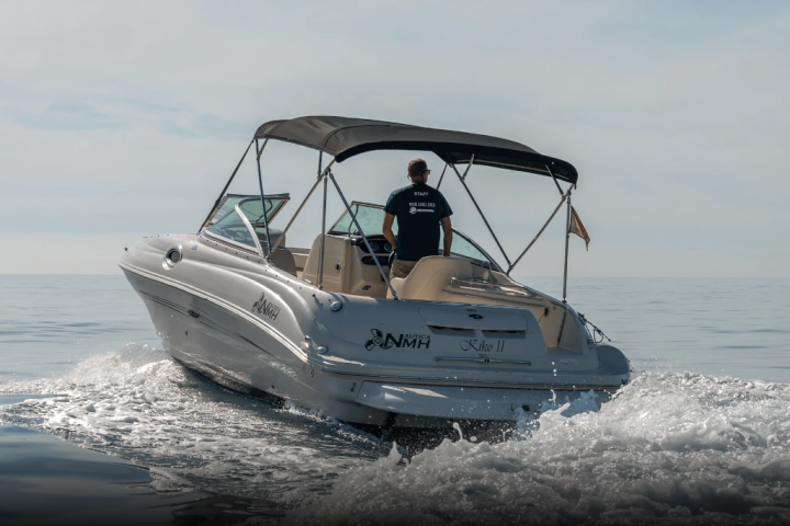 Person piloting a motorboat on calm sea, rear view, with name 'Kiko II' visible on boat.