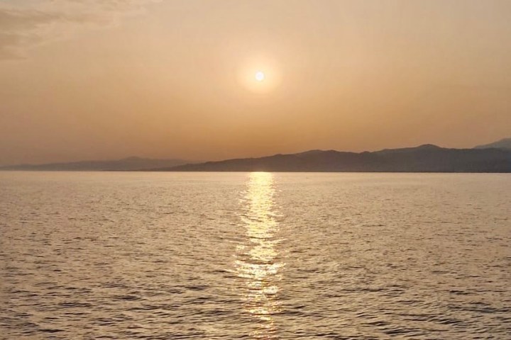 Sunset over calm sea with distant mountains and clear sky.