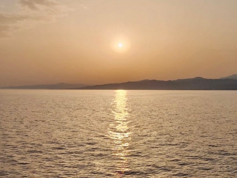 Sunset over calm sea with distant mountains and clear sky.